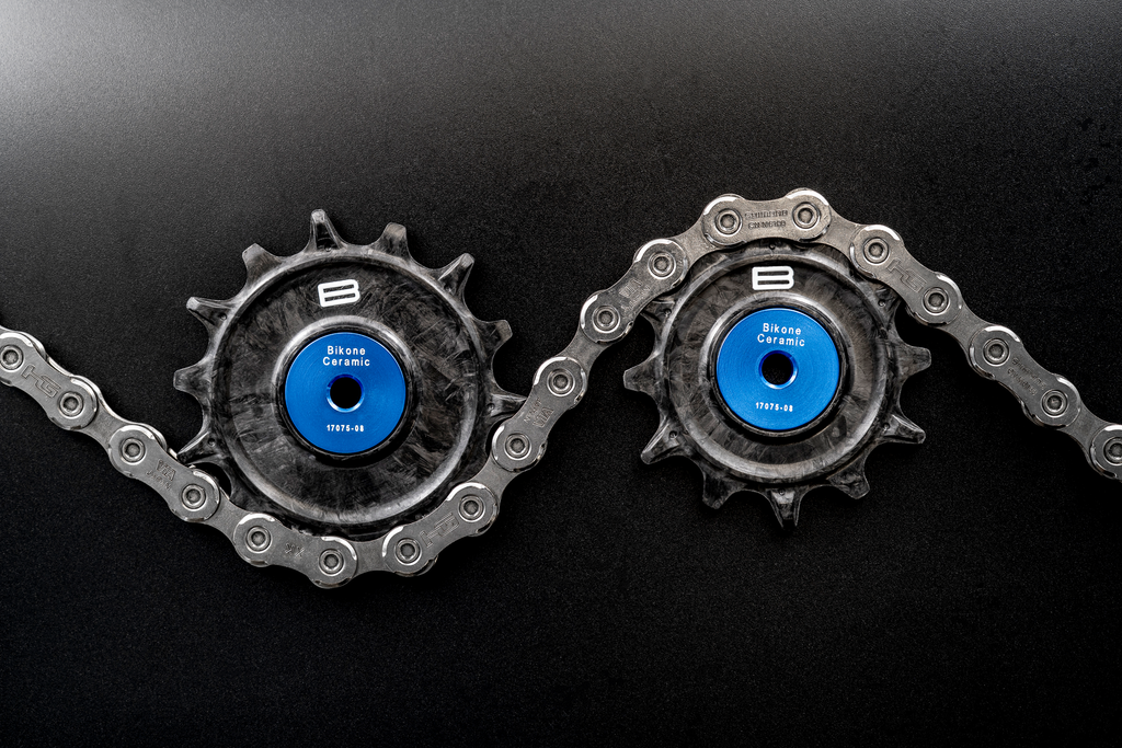 Bikone Forged Carbon Pulley Wheels, upper and lower pulleys threaded through a chain on a black background, road bike drivetrain components