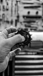 Bikone Forged Carbon Pulley Wheels, pulley held in a mechanic's hand in a workshop, black and white, road bike drivetrain components